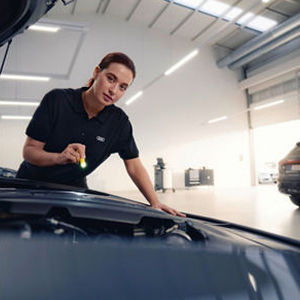 A mechanic in red overalls with Audi logo changing a car's oil