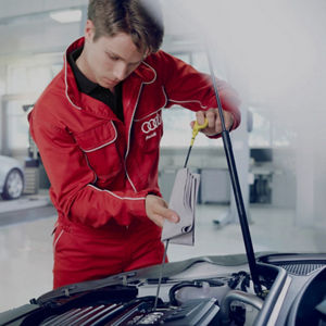 A mechanic in red overalls with Audi logo changing a car's oil