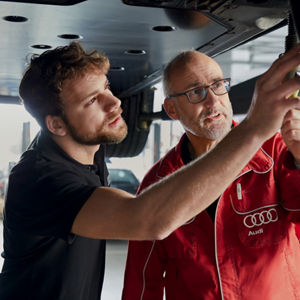 Two mechanics standing underneath a car