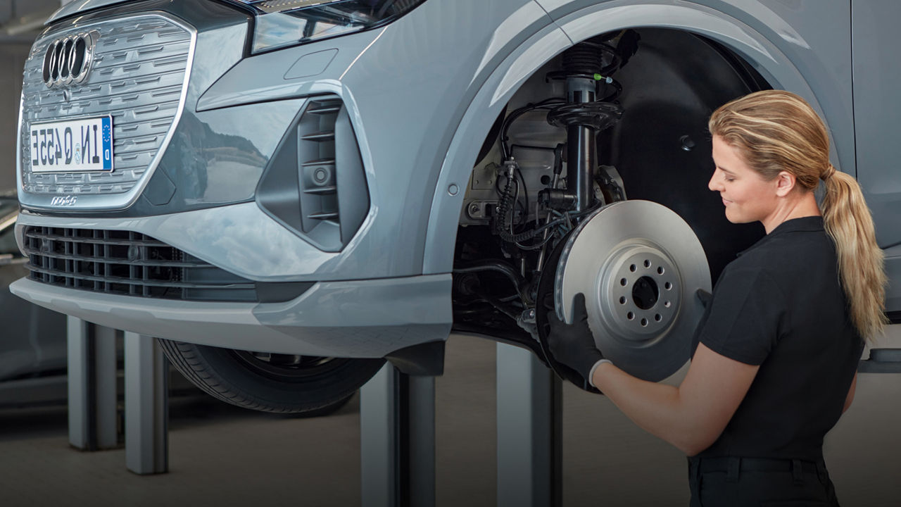 An Audi mechanic tending to the wheel hub of a raised Audi vehicle and an Audi service centre