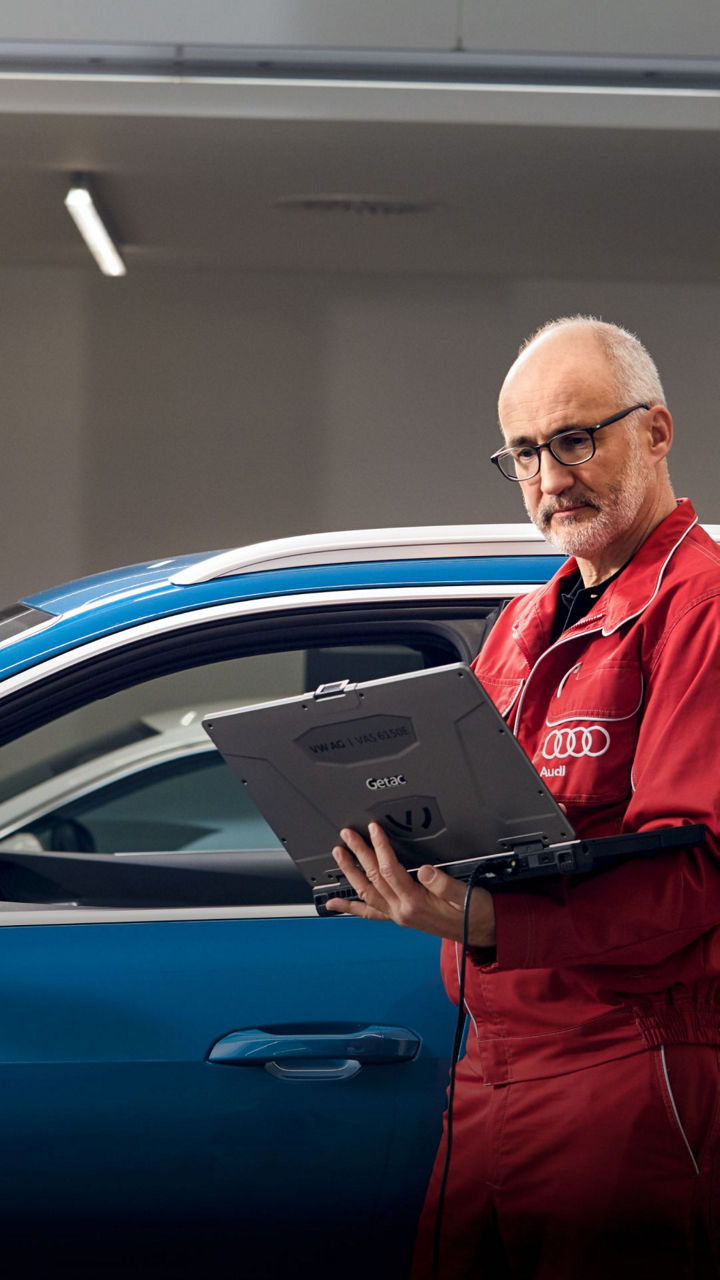 Audi Technician in front of a vehicle, holding a laptop