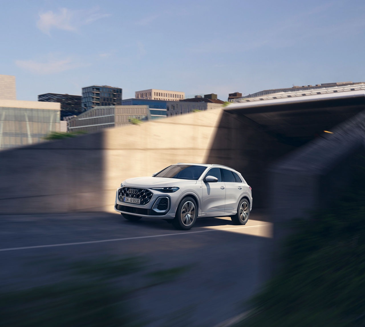 A white Audi Q5 SUV navigates a modern, shadowy urban environment, showcasing its stylish design and dynamic movement. 