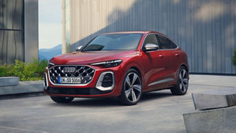 A sleek red Audi SQ5 parked in a modern urban setting with glass buildings and greenery in the background, showcasing its stylish design.