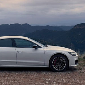 A silver Audi is parked on a dirt road overlooking distant, misty mountains. The scene conveys a sense of tranquility and adventure.