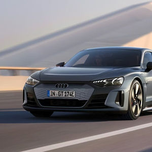 A silver Audi car speeds along a smooth road, evoking a sense of power and elegance. The scene is dynamic with a blurred background.