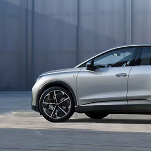 A Silver Audi SUV parked in front of a sleek glass building. The focus is on the car's side profile, highlighting its modern design and alloy wheels.