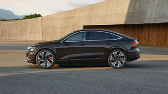 A black Audi vehicle parked outdoors with a modern structure in the background