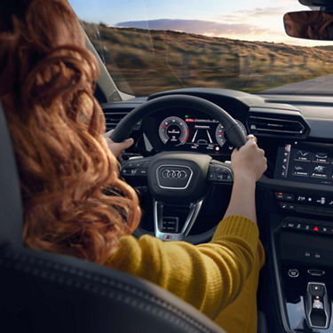 Frau mit beiden Händen am Lenkrad eines Audi A3 allstreet; digitales Cockpit und zentrales Touchdisplay sichtbar.