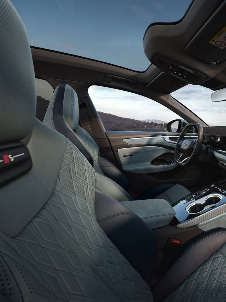 Das Bild zeigt den Innenraum des Audi A6 Avant e-hybrids. Der Innenraum verfügt über ein modernes Armaturenbrett mit integrierten Touchscreen-Displays für Navigation und Fahrzeugbedienung. Die Sitze sind mit einem charakteristischen Rautenmuster genäht. Das Interieur ist in Grau- und Blautönen gehalten.