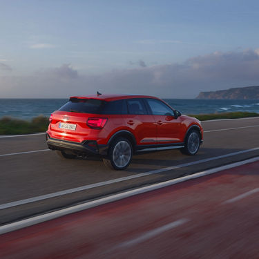 Ein roter Audi SQ2 fährt auf einer Küstenstraße am Meer entlang. Weiter hinten sieht man eine Klippe.