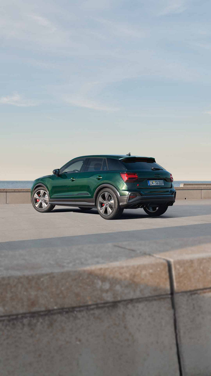Ein dunkelgrüner Audi SQ2 auf einem betonierten Platz vor dem Meer, Fahrzeug von schräg hinten gezeigt bei Tageslicht.