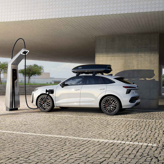 Audi Q3 Sportback vista di lato mentre si ricarica a una colonnina pubblica. L’auto bianca si trova in un parcheggio con un box nero sul tetto.