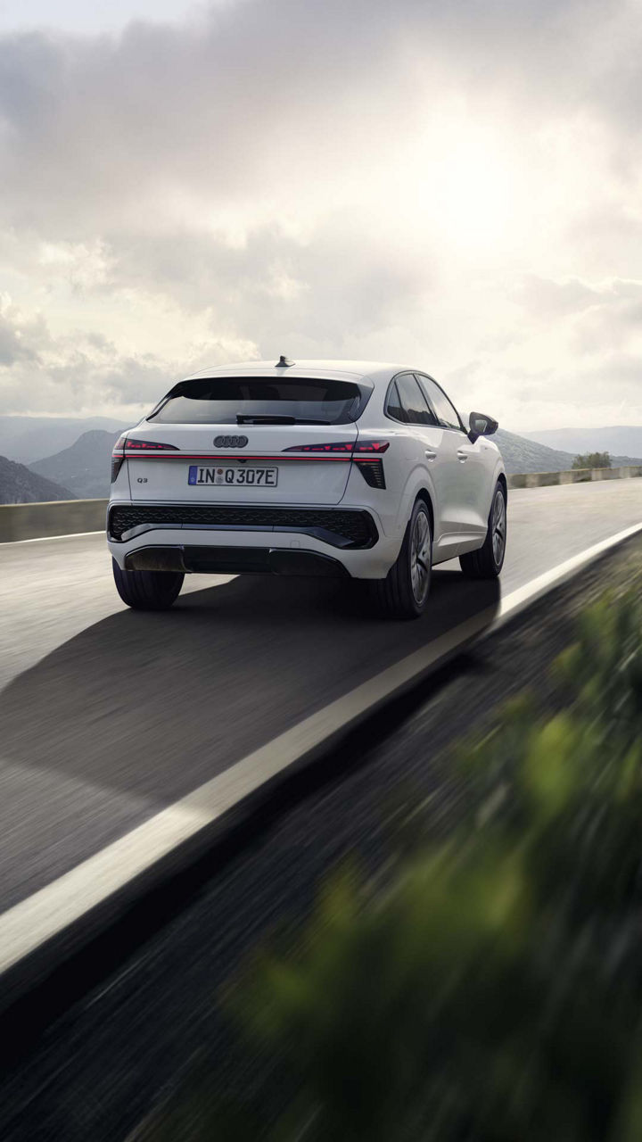 Ein weißer Q3 Sportback e-hybrid fährt auf einer Landstraße in einer bergigen Landschaft.