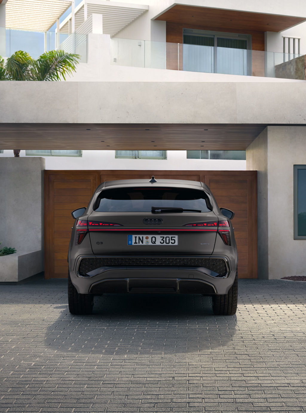 The Audi Q3 Sportback can be seen from the rear view. It is parked in front of a wooden entrance gate to a residential building.