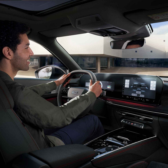 Audi Q3 Sportback von Innen. Zu erkennen ist ein Mann der im Auto auf dem sitz sitz und das Lenkrad in der Hand hält. Weiterhin erkennt man das Panorama Display auf dem verschiedenen sitz Einstellungen zu sehen sind.