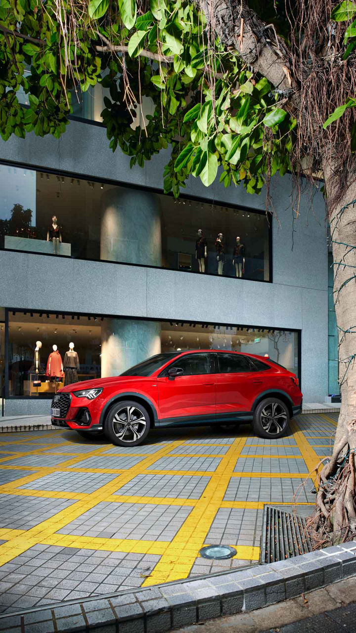Ein roter Audi Q3 Sportback parkt vor einem Modegeschäft mit beleuchtetem Schaufenster und Schaufensterpuppen.