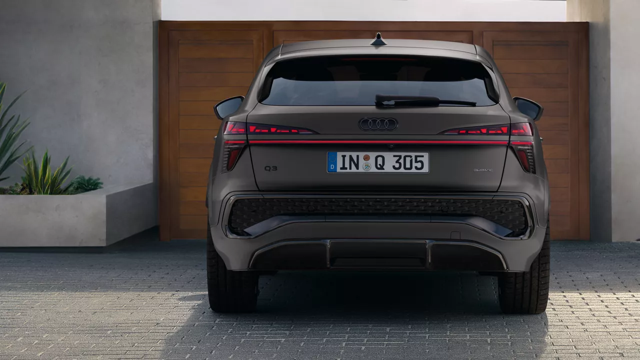 Blick von hinten auf den Q3 Sportback, der vor einer hölzernen Eingangstür parkt.