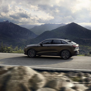 The Q3 Sportback drives along a country road in a mountainous landscape.