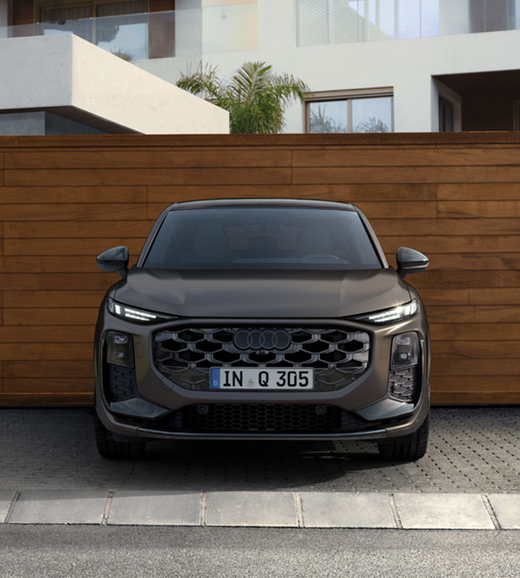The Q3 Sportback is parked in front of a modern building, with a wood-effect wall behind it.