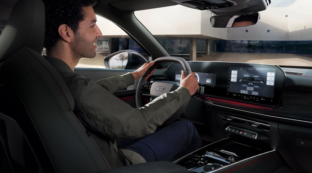 View from behind at an angle of the cockpit of the Q3 Sportback, a young man is sitting at the wheel.