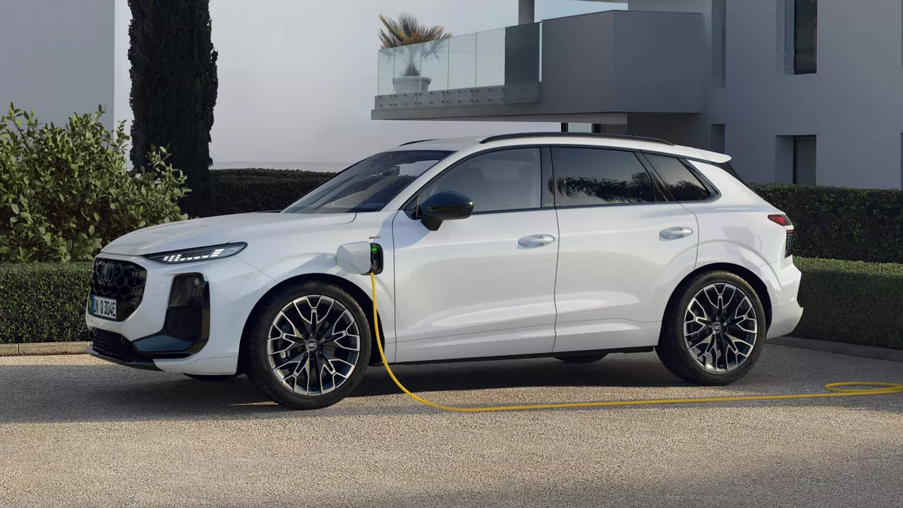 Side profile of a white Q3 SUV e-hybrid charging in the parking lot in front of a modern house.