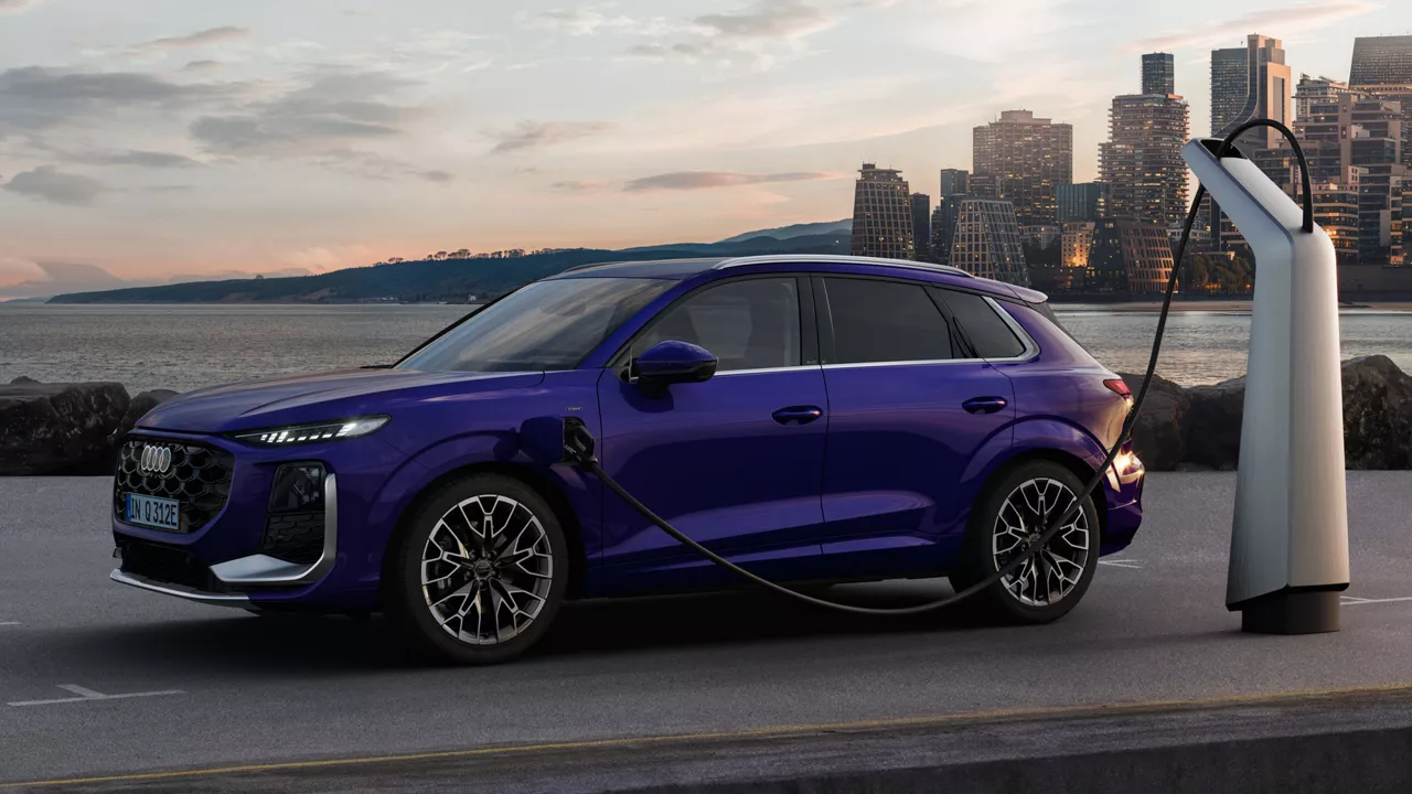 A Q3 SUV e-hybrid in velvet violet pearl effect at a charging station, with the skyline of a coastal city in the background.