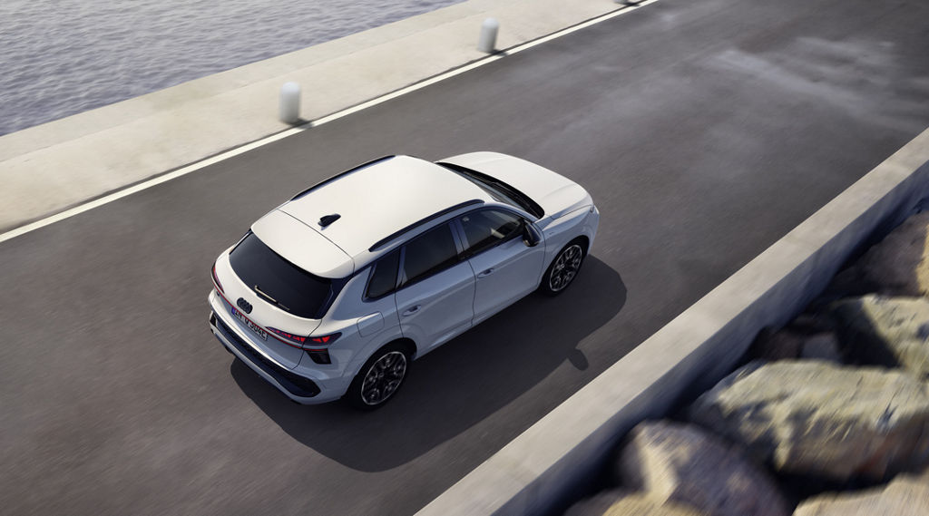 The Q3 SUV e-hybrid drives along a road parallel to the sea. 	
