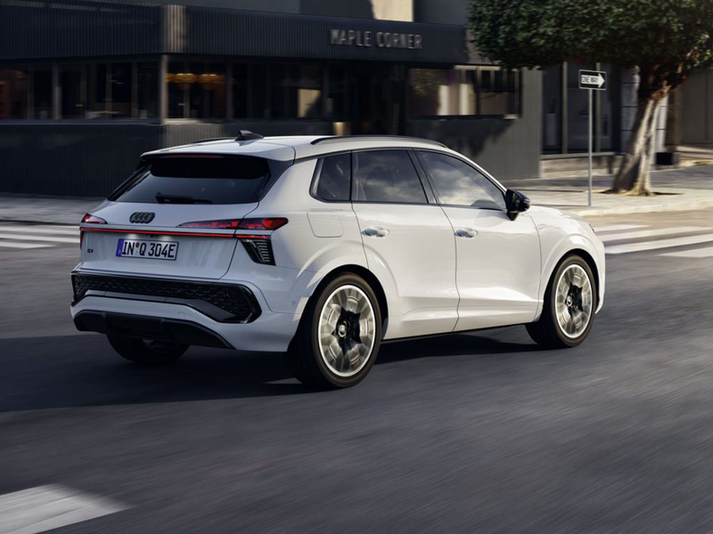 A white Q3 SUV e-hybrid seen from the rear right while driving at an intersection in the city center.	
