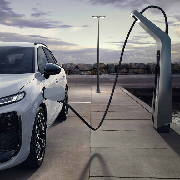 Balts Q3 SUV e-hybrid pie uzlādes stacijas tukšā autostāvvietā.