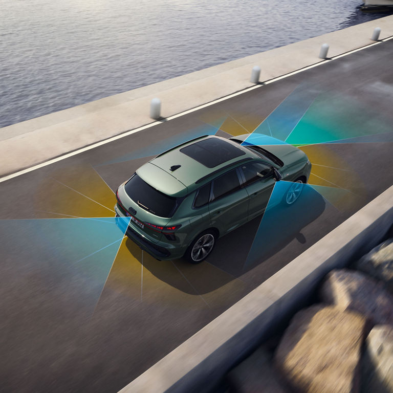 Das Bild zeigt einen grünen Audi Q3 SUV, der auf einer Straße neben einem Gewässer fährt. Vom Auto gehen farbige Strahlen aus, die eine Sensorik oder eine Sicherheitsfunktion illustrieren. Das hintere Nummernschild ist sichtbar, und das Auto hat ein Panorama-Schiebedach. Der Gesamteindruck vermittelt den Eindruck, dass der Schwerpunkt auf fortschrittlicher Fahrzeugtechnologie und Design liegt.