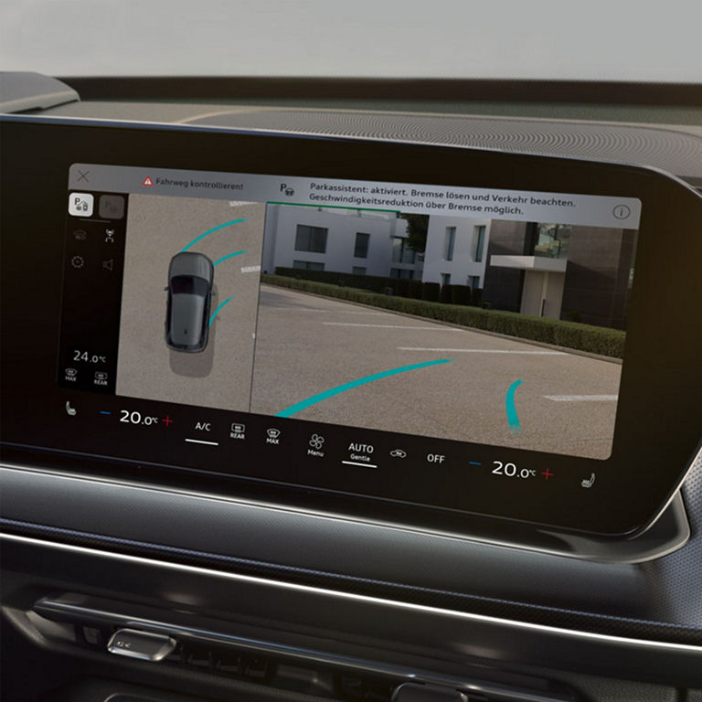 Das Bild zeigt den Infotainment-Bildschirm des Fahrzeugs, auf dem die Funktion „Parkassistent“ aktiviert ist. Eine Nachricht fordert dazu auf, die Bremse zu lösen.  Auf dem Bildschirm erscheint außerdem die Warnung „Fahrweg kontrollieren!“, begleitet von einer Draufsicht auf das Fahrzeug und seine Umgebung mit blauen Führungslinien. Am unteren Rand des Bildschirms sind Bedienelemente für Klimaanlage, Sitzheizung und Automatikmodus sichtbar.