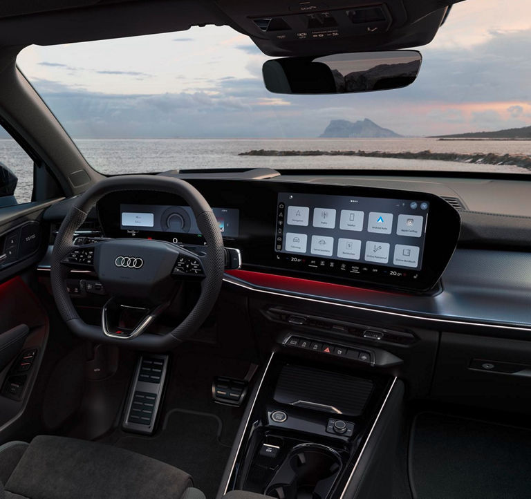 Das Bild zeigt das Innere eines Audi mit Blick auf das Meer und eine Landformation im Hintergrund. Das Auto verfügt über ein digitales Armaturenbrett, auf dem Optionen für Navigation, Radio, Telefon und Fahrzeugeinstellungen angezeigt werden. Ein SONOS-Soundsystem ist in die Türverkleidung des Fahrzeugs integriert. Das Armaturenbrett zeigt 45 km und 5,4 APEAG sowie verschiedene Bedienelemente für Fahrzeugeinstellungen und Fahrhilfen an und unterstreicht damit den Fokus auf Technologie und Komfort.