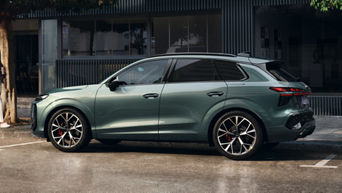 Audi Q3 verde con la portiera aperta su una strada bagnata accanto a un edificio.  L’architettura moderna dell’edificio crea uno sfondo contemporaneo per la scena.