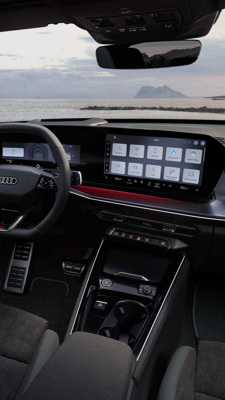 Rear view of the cockpit of the Q3 Sportback with steering wheel, panoramic display, and red ambient lighting package. The sea can be seen through the windshield.