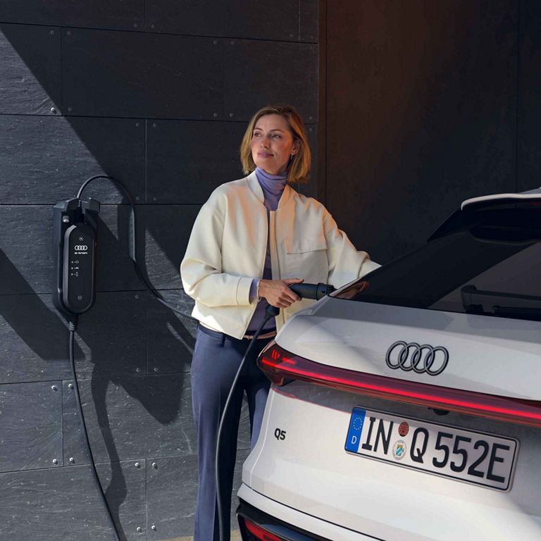 A woman charges an Audi Q5 Sportback e-hybrid at home 