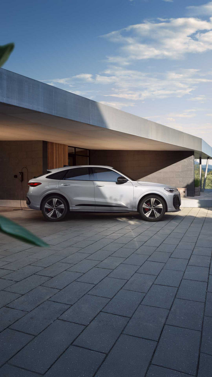 A white Audi Q5 Sportback e-hybrid side view in front of a house