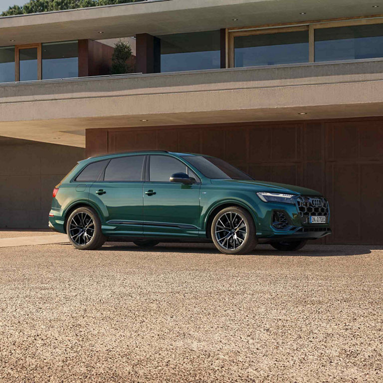 Ein dunkelgrüner Q7 SUV parkt vor einem modernen Haus. Daneben steht ein modern angezogener Mann.