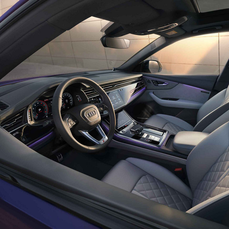 Innenraum eines Audi Q8 SUV in velvet lila mit  weißen Leder-Sportsitzen, großem Touchdisplay, Lenkrad und digitalem Cockpit.