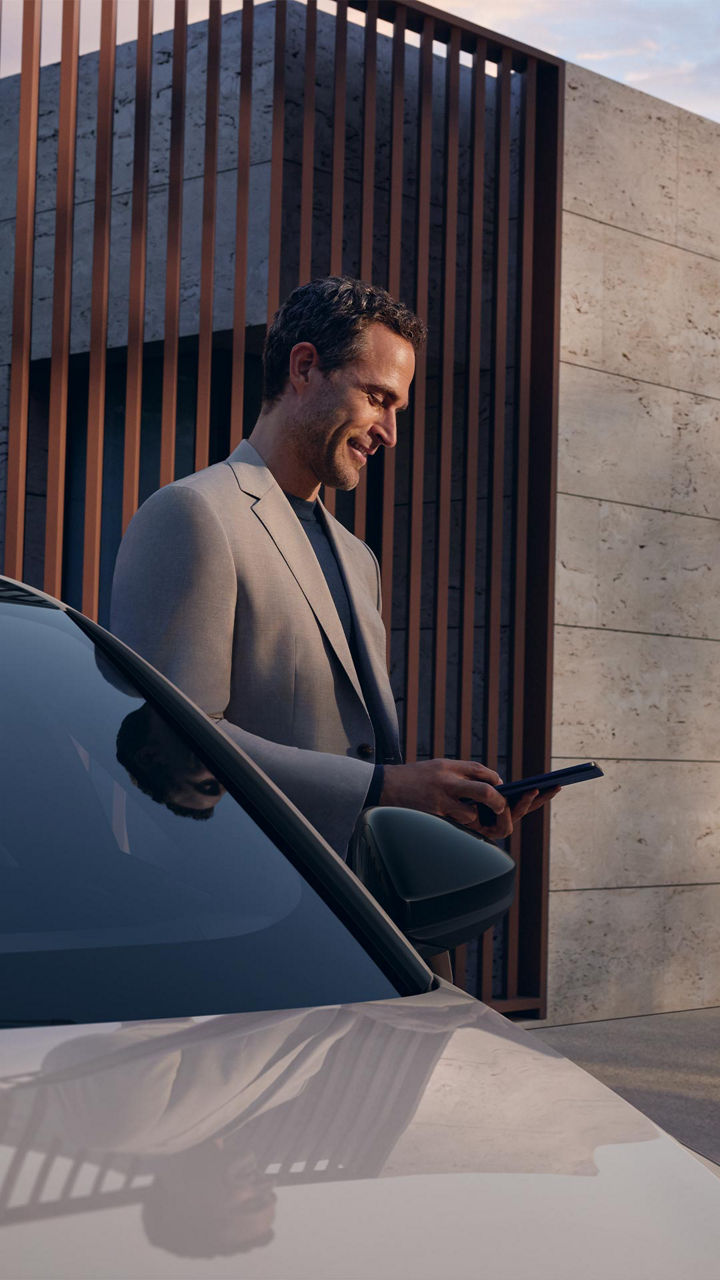 un uomo, in piedi a fianco della propria Audi, consulta lo smartphone