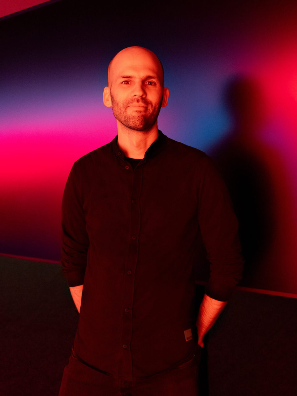 Portrait von Audi Designer Christoph Häußinger vor einer in rotes  und blaues Licht getönten Wand. 