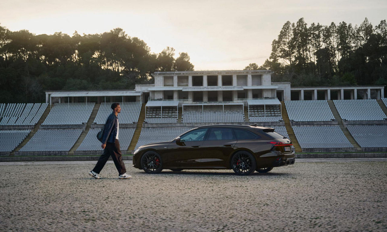 Leo Neugebauer läuft auf einen in einem Stadion geparkten Audi A6 Avant zu.