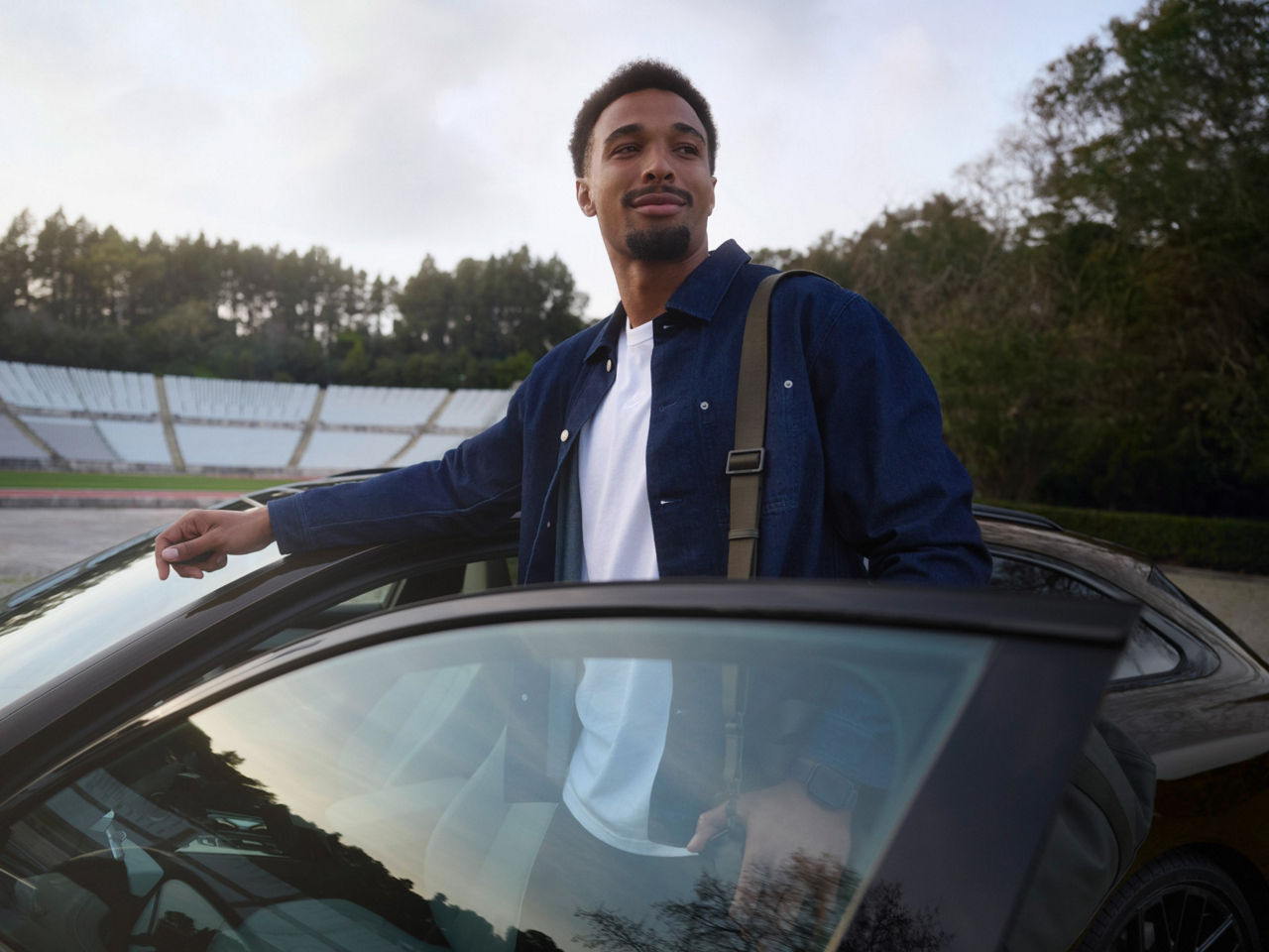 Leo Neugebauer steht in der geöffneten Fahrertür eines Audi A6 Avant, der in einem Stadion geparkt ist.