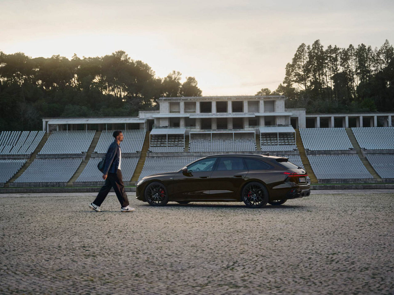 Leo Neugebauer läuft auf einen in einem Stadion geparkten Audi A6 Avant zu.
