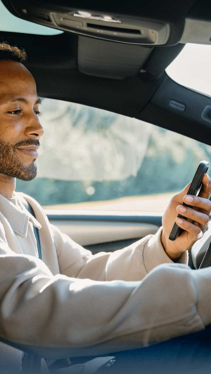 Een man zit in een auto, houdt een smartphone in de ene hand en bedient met de andere hand het touchscreen-display op het dashboard.