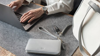A woman is working on a laptop (only her hands can be seen), on the table are an Audi key, a beige bag and a gray wallet with the Audi logo
