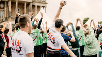 Cheering crowd outside with raised hands and AIA t-shirts or green t-shirts/jackets at a festival/concert