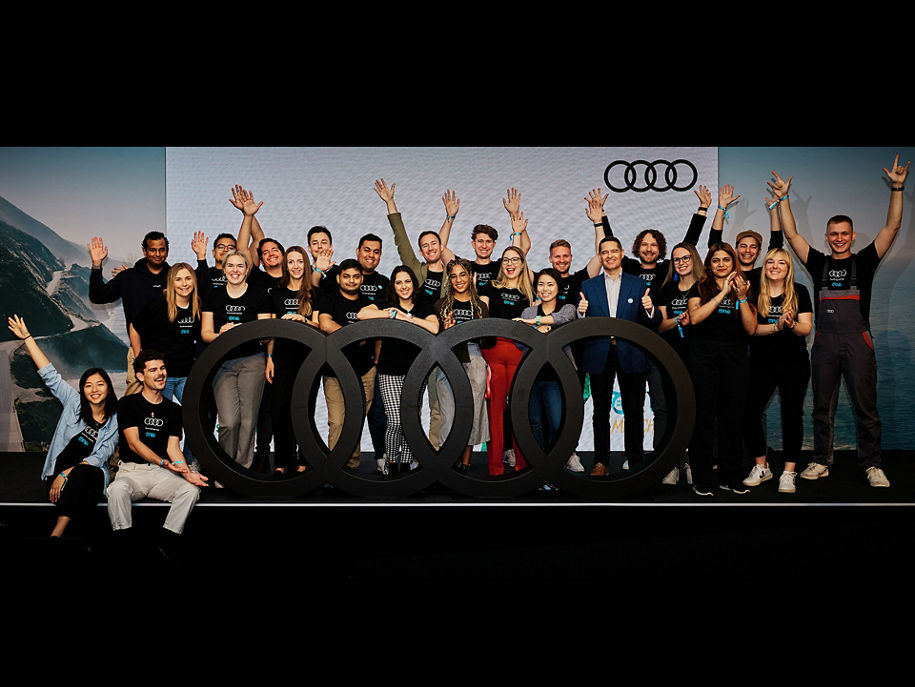Many people stand cheering on a stage around the Audi rings