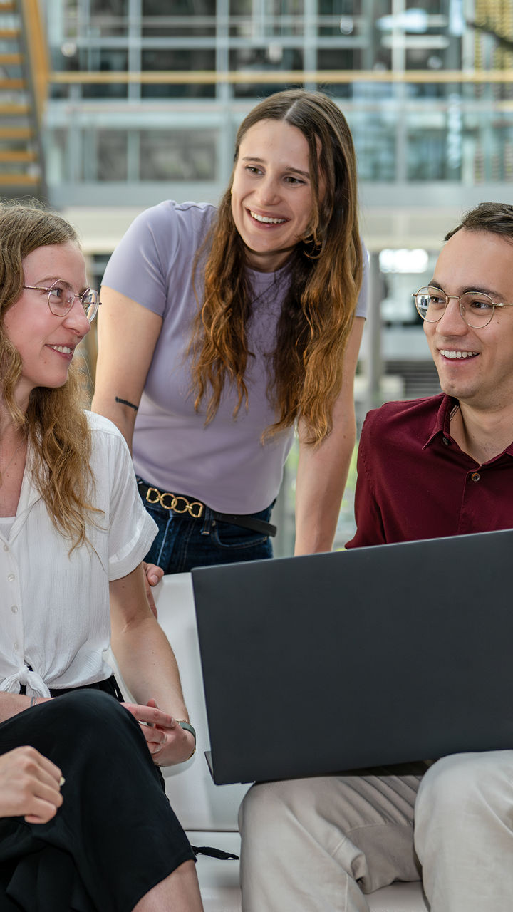 Four graduates look at each other, smile, and have a laptop in front of them