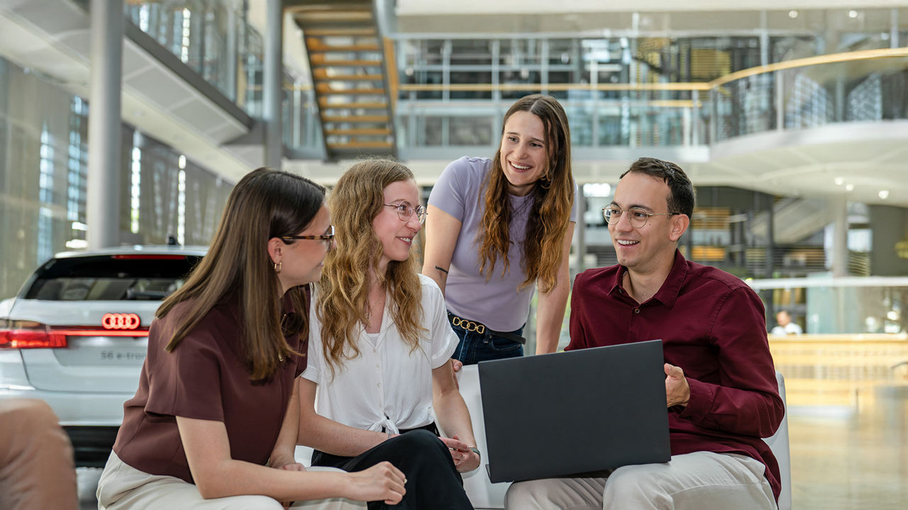 Four graduates look at each other, smile, and have a laptop in front of them