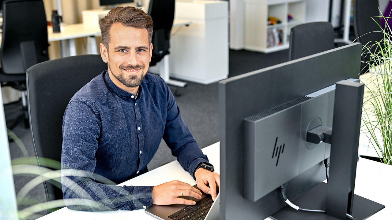 Markus, Product Manager SCD, sitzt am Laptop und lacht in die Kamera